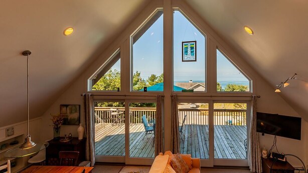 A spacious room with a large window, a wooden dining table, a sofa, and a TV mounted on the wall.