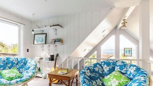 A room with two blue and white patterned chairs, a small wooden table, and a view of the sea through large windows.