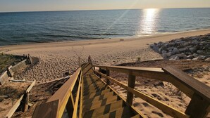 A wooden staircase leading to a beach with a clear view of the ocean and the sun setting in the background.