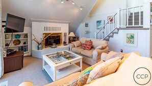 A cozy living room with a fireplace, a sofa, a coffee table, and a staircase.