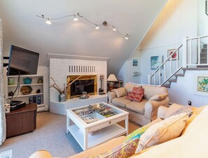 Un salon chaleureux avec une cheminée, un canapé, une table basse et un escalier.