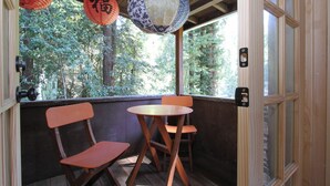 A traditional Japanese room with tatami flooring, a wooden table, two chairs, and a view of a forest through a sliding door.
