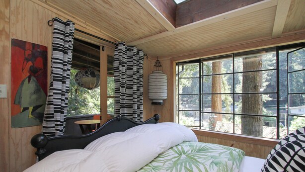 A bedroom with a bed, a window with a view of trees, a hanging lantern, and a painting on the wall.