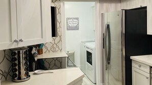 Una cocina moderna con armarios blancos, un refrigerador de acero inoxidable y una encimera de mármol.