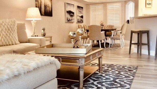 Una sala de estar con un sofá, una mesa de centro y objetos decorativos. Se observa un comedor con sillas y una mesa al fondo.