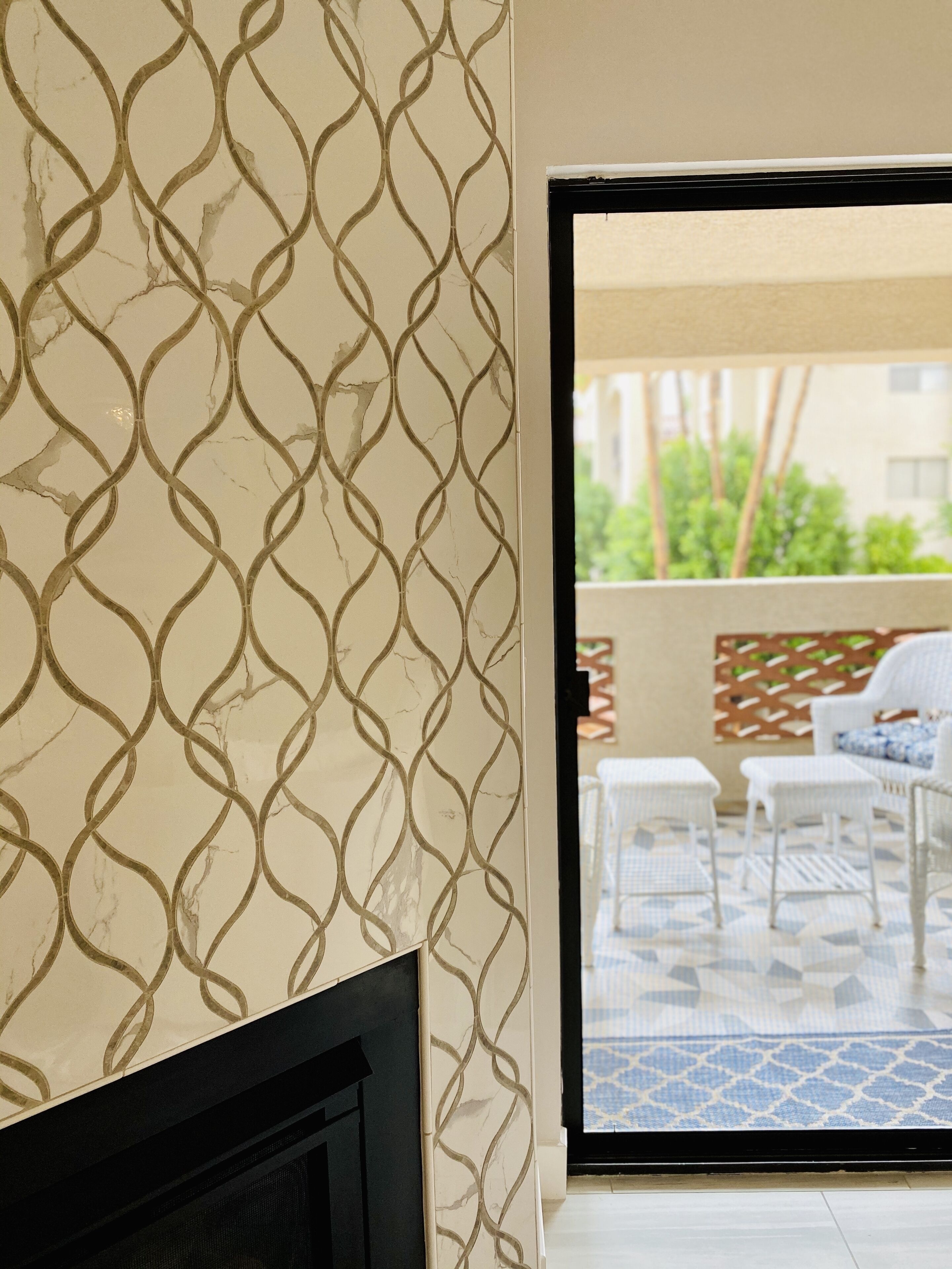 A room with a patterned wall, a fireplace, and a view of an outdoor patio with a table and chairs.