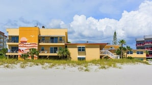 Ein Strandhotel mit mehreren Balkonen, einem Sandstrand davor und einem klaren Himmel.
