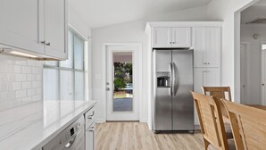 Una cocina moderna con armarios blancos, un refrigerador de acero inoxidable y una mesa de comedor de madera.