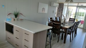 Et spiseområde med et langt bord og flere stole, et køkken med skabe og en bordplade, samt et vindue med gardiner.