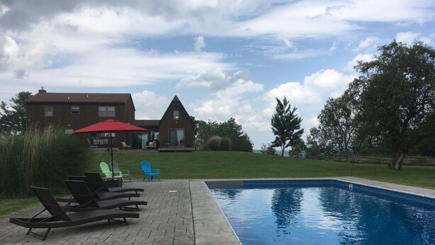 Ein Pool mit Liegestühlen und einem roten Sonnenschirm, umgeben von einer Ziegelterrasse und einer Rasenfläche.