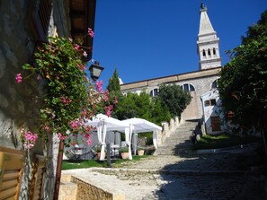 A cobblestone street leading to a historic building with a tower. There are white tents set up along the path, suggesting an event or gathering.