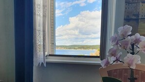 Ett bord med en blommig tekanna, två koppar och en vas med orkidéer, placerat vid ett fönster med utsikt över havet och molnen.