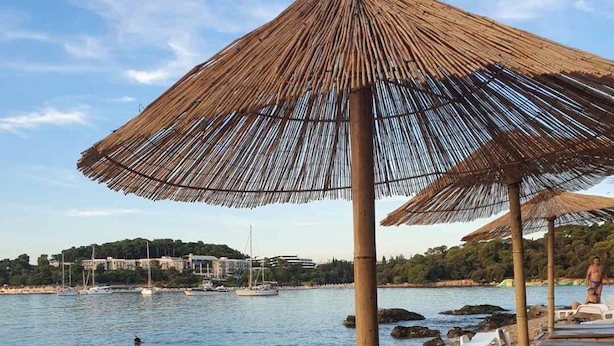 En strand med parasoller av halmtak och solstolar.