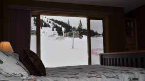 Une chambre d’hôtel avec un lit, une fenêtre donnant sur une montagne enneigée et un télésiège, ainsi qu’une bibliothèque.