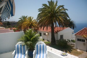 A terrace with two striped lounge chairs, a palm tree, and a building with a red-tiled roof. - Paradise tranquility. Sea and Teide views (La Victoria de Acentejo)