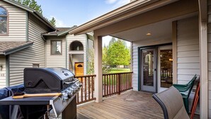 A covered deck with a grill, a chair, and a view of the house. - Welcome to The Explorers Den, Mountain Harbor #147 (Whitefish)