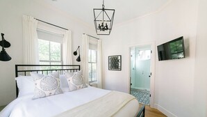 A bedroom with a large bed, a chandelier, a TV, and a glass shower door.