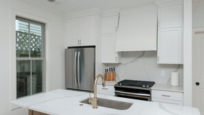 A modern kitchen with white cabinetry, a stainless steel refrigerator, a gas stove, and a marble countertop.