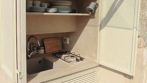 Uma cozinha compacta com pia, fogão e prateleiras com louças e uma xícara.
