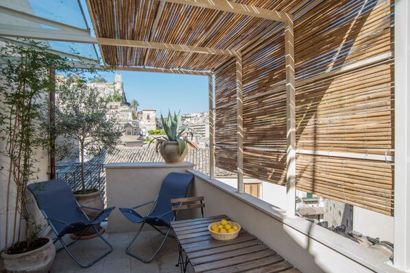 A balcony with two blue chairs, a wooden table, and a potted plant.