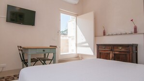Quarto com cama, escrivaninha, televisão, guarda-roupa e janela com vista.
