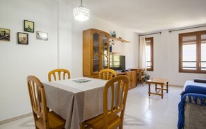 A dining area with a table and chairs, a cabinet with glass doors, a television, and a window with blinds. - MIQUEL 1 – Apartment with Parking and Wi-Fi in the (Tossa De Mar)