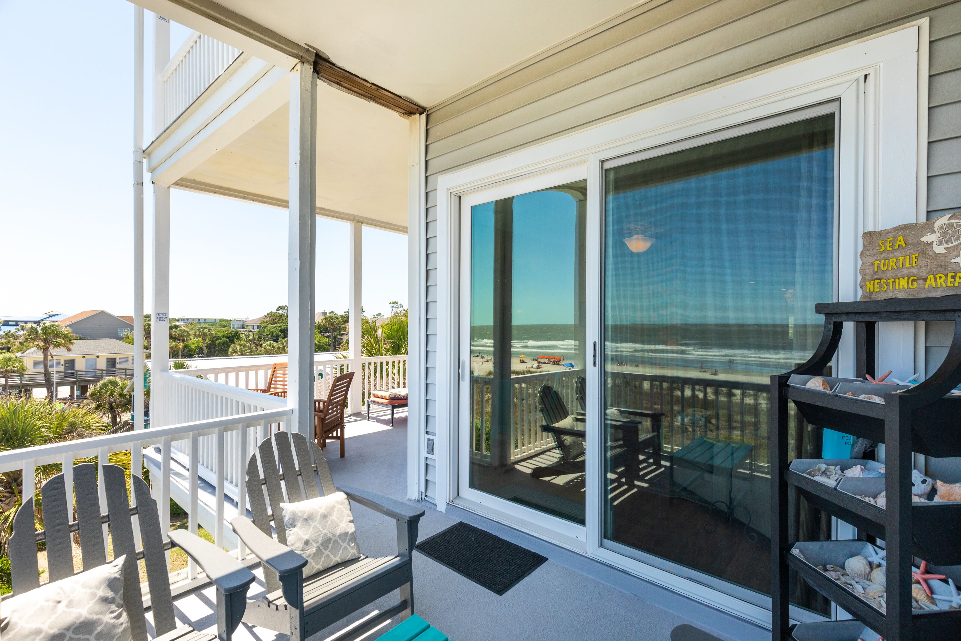 A covered outdoor area with a view of the beach, featuring a seating area with chairs and a table.