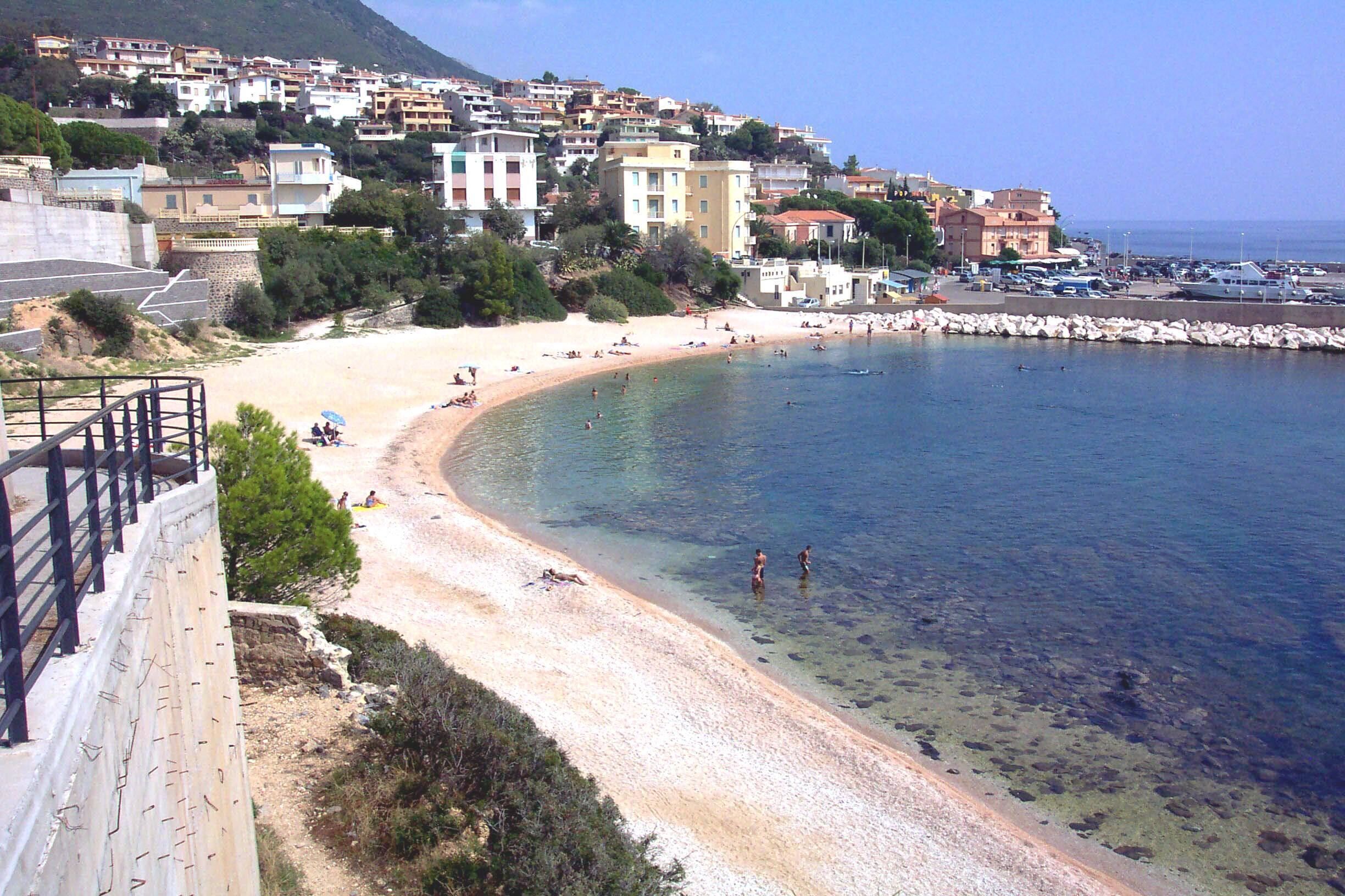 A coastal town with a sandy beach, clear water, and buildings along the shore.