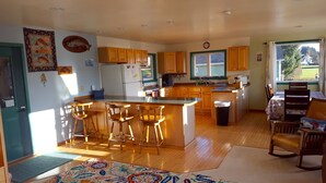 A spacious kitchen with wooden cabinets, a central island with bar stools, a refrigerator, and a window overlooking a green landscape.