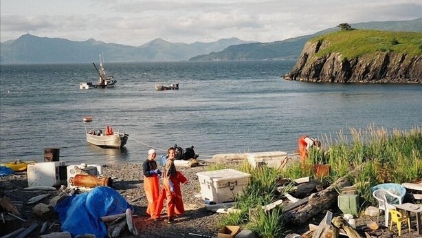 A coastal scene with boats, a rocky shore, and mountains in the background.
