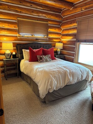 Un dormitorio tipo cabaña de madera con una cama grande, dos lámparas de noche y una ventana con persianas.
