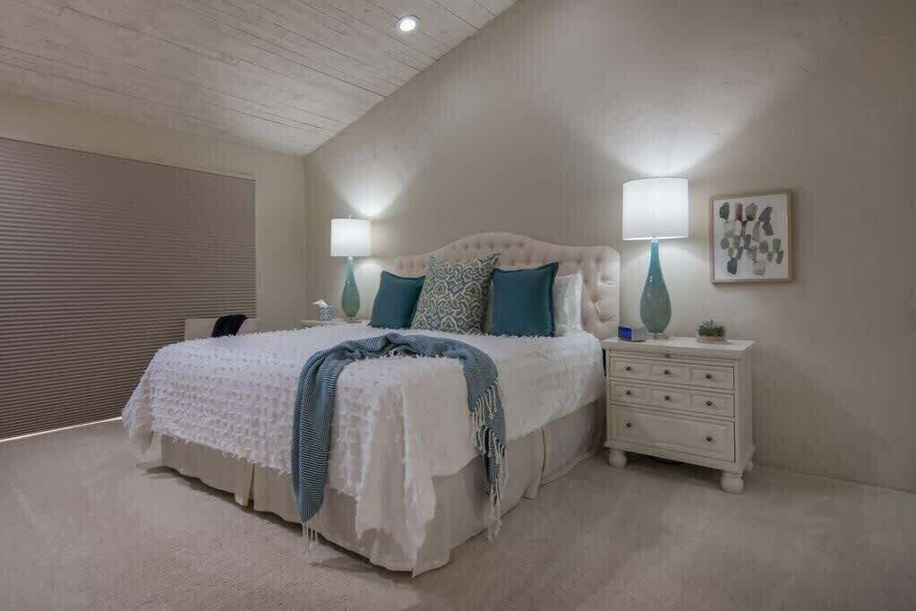 A bedroom with a large bed, two bedside tables, a ceiling light, and a wall-mounted lamp.
