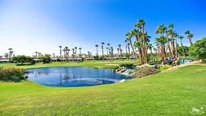 Un campo de golf con un estanque, palmeras y un cielo azul despejado.