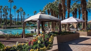 Zona de piscina con palmeras, una piscina y un parterre de flores.