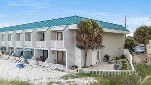 Un motel frente a la playa con varios balcones, una zona de estar al aire libre cubierta y una playa de arena frente a él.