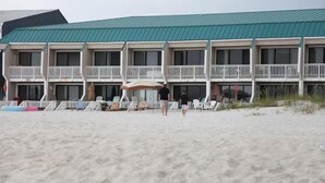 Un hotel frente a la playa con varios balcones, sillas y sombrillas.