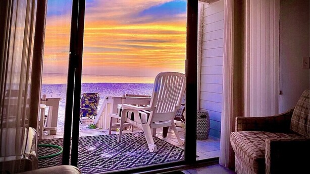 Habitación con puerta de cristal corredera que da a un balcón con vista al océano al atardecer.