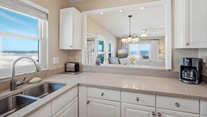 A modern kitchen with a large window, a built-in sink, and a coffee maker. - Bright oceanfront corner 2/2 with beach/pool views, large balcony, and multiple pools (New Smyrna Beach)