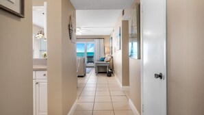 A hallway with a view to the outside, a ceiling fan, and a door with a handle. - Bright oceanfront corner 2/2 with beach/pool views, large balcony, and multiple pools (New Smyrna Beach)