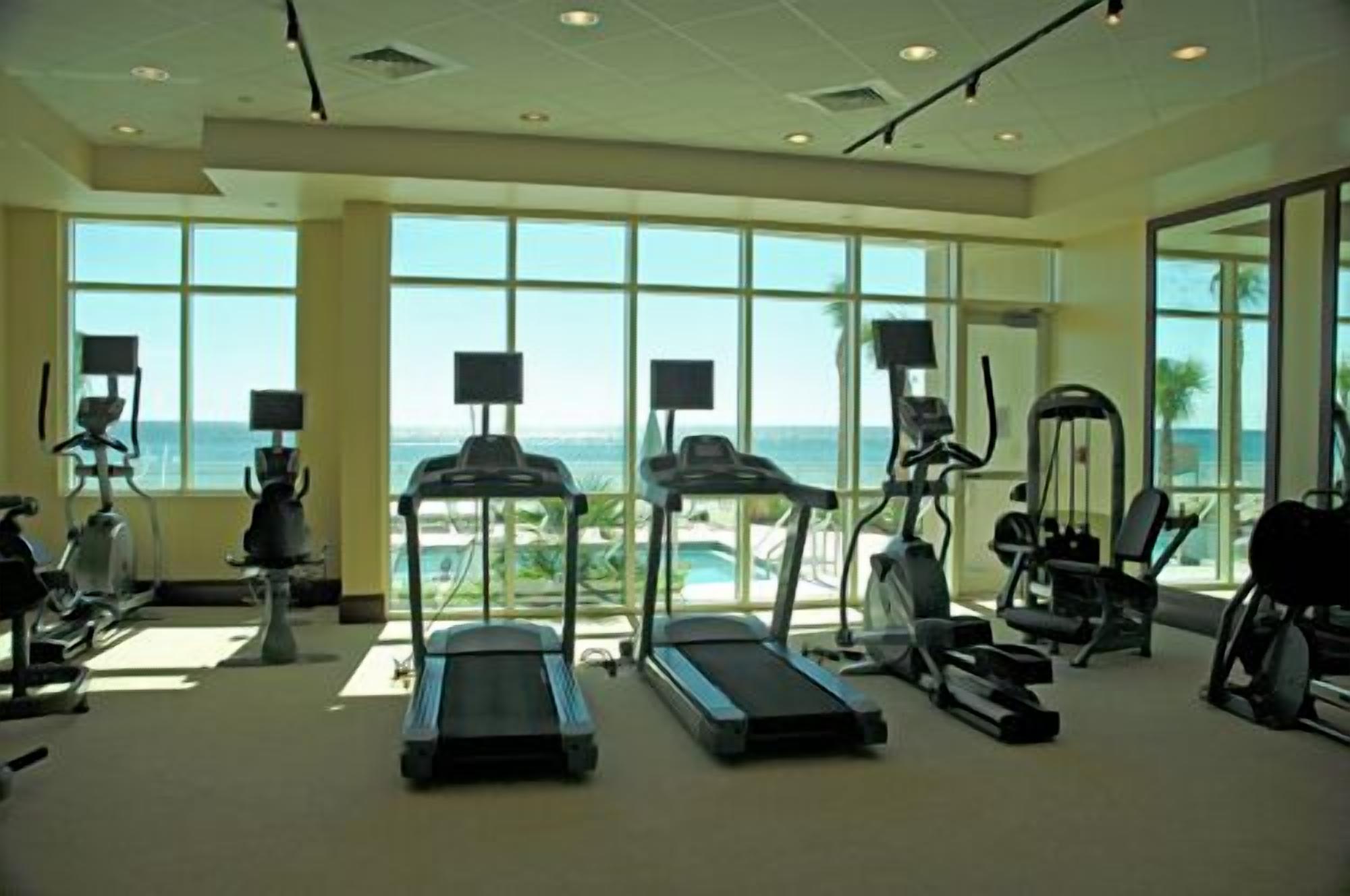 Une salle de sport équipée de tapis de course, d’appareils elliptiques et de vélos d’exercice, et dotée de grandes fenêtres offrant une vue sur l’océan.