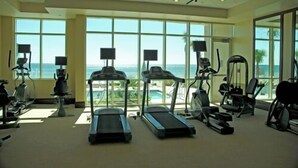 Et fitnesscenter med løbebånd, crosstrainere og motionscykler, med store vinduer og udsigt over havet.