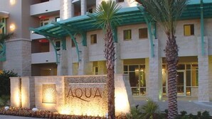 Et flere etagers hotel med et markant 'AQUA' skilt, palmer og en stenfassade.