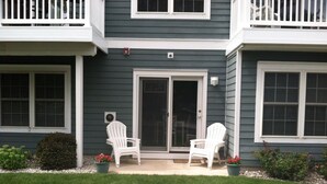Ein zweistöckiges Gebäude mit einer Veranda, zwei weißen Adirondack-Stühlen und einem kleinen Garten mit roten Blumen.