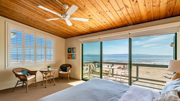 A bedroom with a large bed, a ceiling fan, and a view of the beach through large windows. - Seahorse Retreat - Double The Fun, BEACHFRONT, In Carpinteria! (Carpinteria)