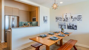 A modern kitchen with a built-in island, wooden dining table, benches, and black-and-white artwork on the walls. - Seahorse Retreat - Double The Fun, BEACHFRONT, In Carpinteria! (Carpinteria)