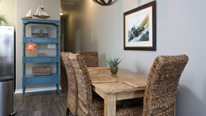 A dining area with a wooden table and wicker chairs, a blue sideboard with decorative items, and a framed picture on the wall. - Read Our Reviews Gorgeous 2 BR Poolside T/h, 3 minute walk to beach! (Corpus Christi)