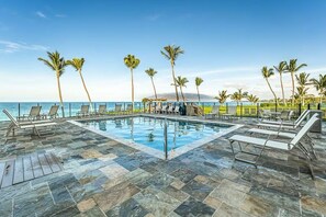 A poolside area with lounge chairs and palm trees, overlooking the ocean.