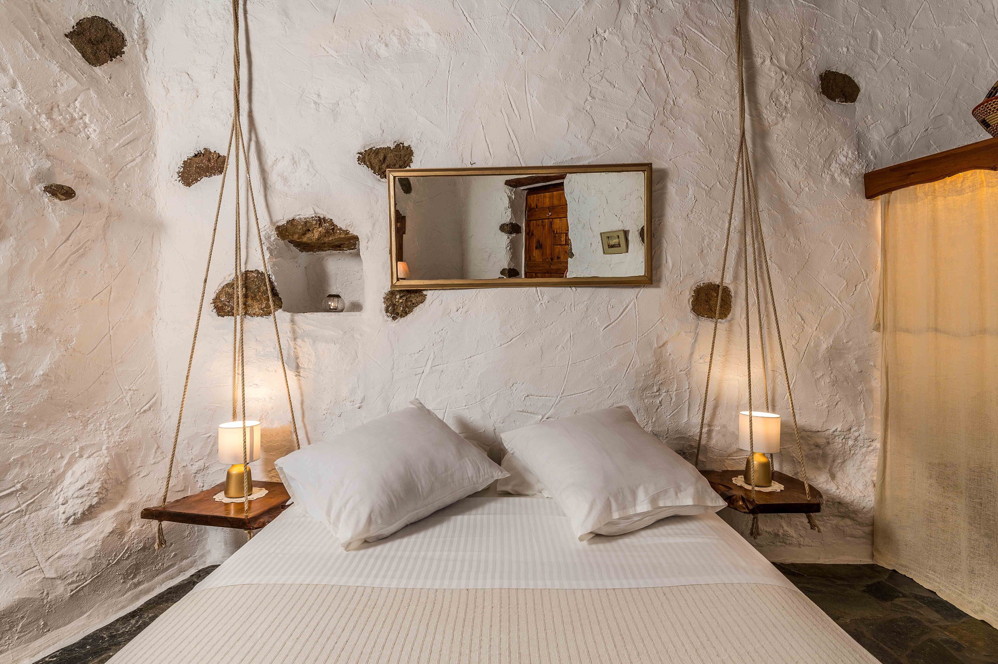 Ein Schlafzimmer mit einem großen Bett, zwei Nachttischen mit Lampen, einem hängenden Spiegel und einer rustikalen Wand.