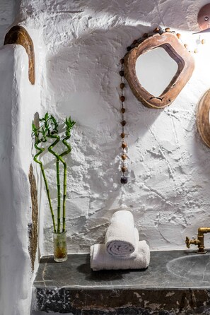 Ein Badezimmer mit einem rustikalen Steinsink, einem weißen Handtuch, einem Spiegel und einem dekorativen Holzstück an der Wand.