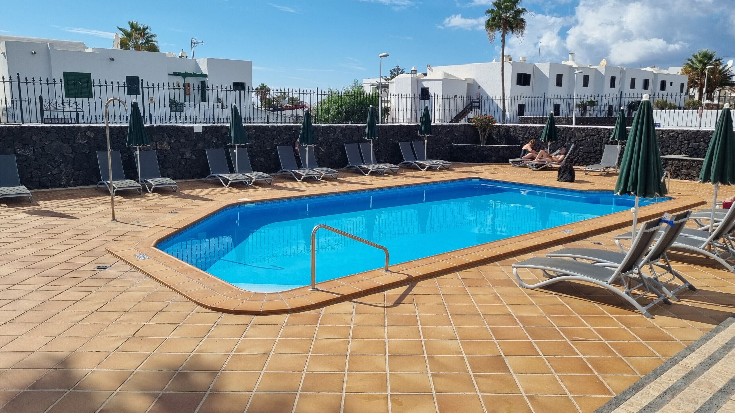 Une piscine rectangulaire, bordée d’une terrasse carrelée, entourée de chaises longues et de parasols.